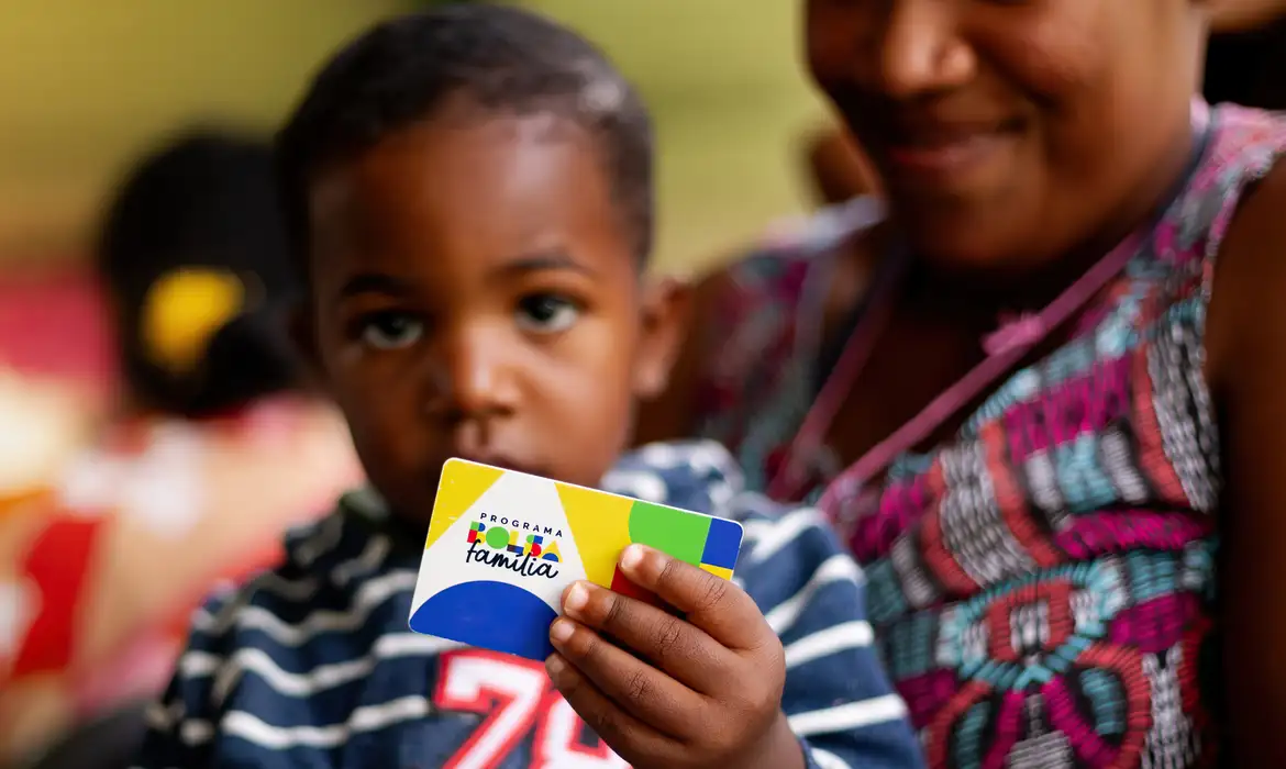 Imagem de uma mãe e o seu filho segurando o cartão do bolsa família 