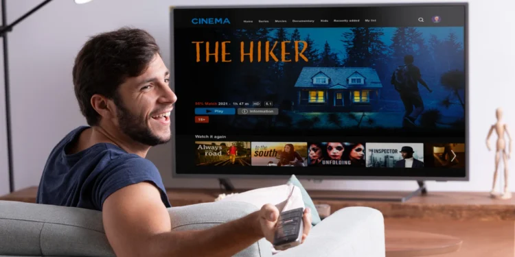 Homem assistindo a filme em uma TV digital com controle remoto na mão.
