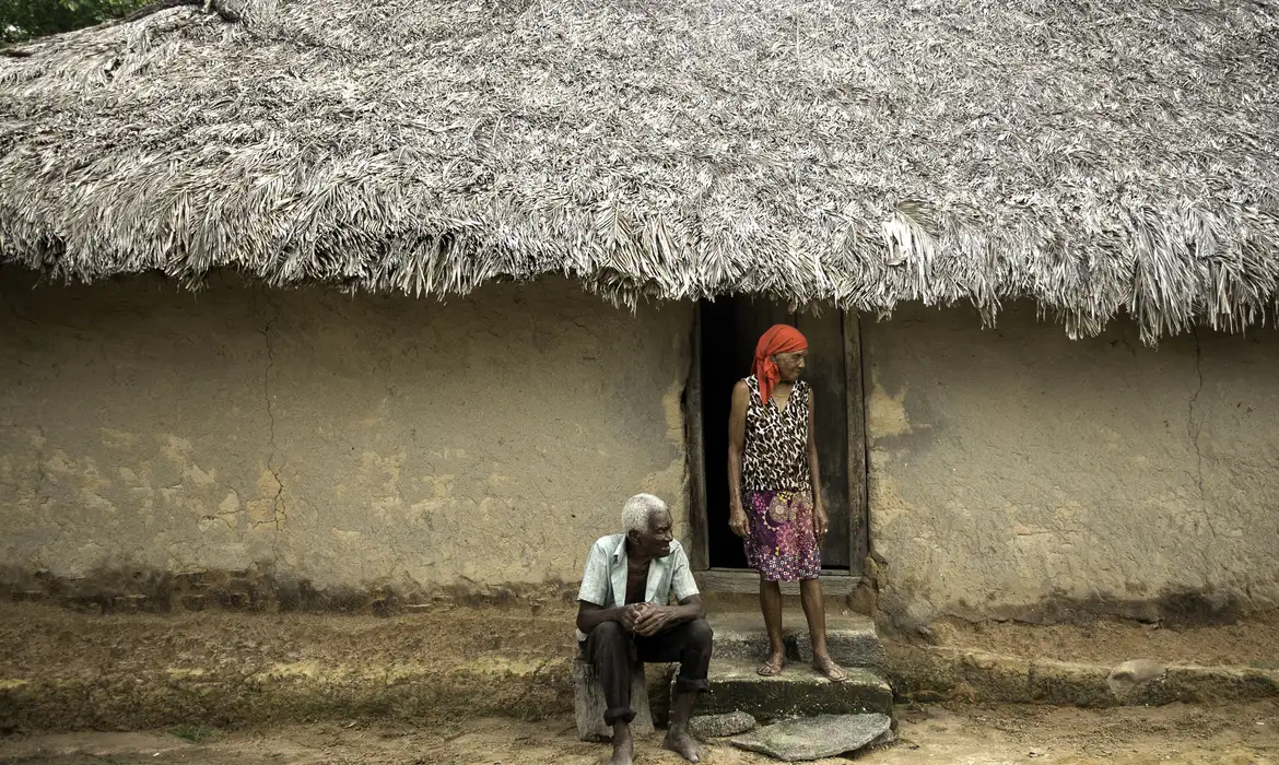 Família quilombola reunida em frente a uma casa simples iluminada por uma lâmpada, simbolizando a importância da Tarifa Social.