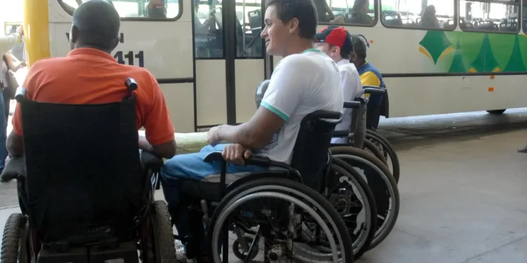 Pessoas em cadeiras de rodas aguardando transporte público, em um ponto de ônibus acessível.