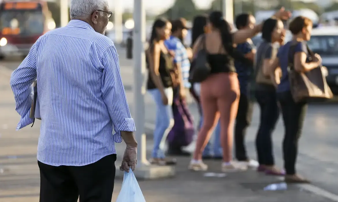 Idoso aguardando transporte em ponto de ônibus, representando beneficiários que ainda precisam realizar a prova de vida presencial.