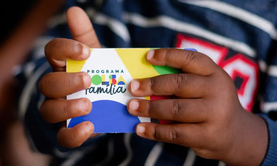 Criança segurando um cartão do Programa Bolsa Família.