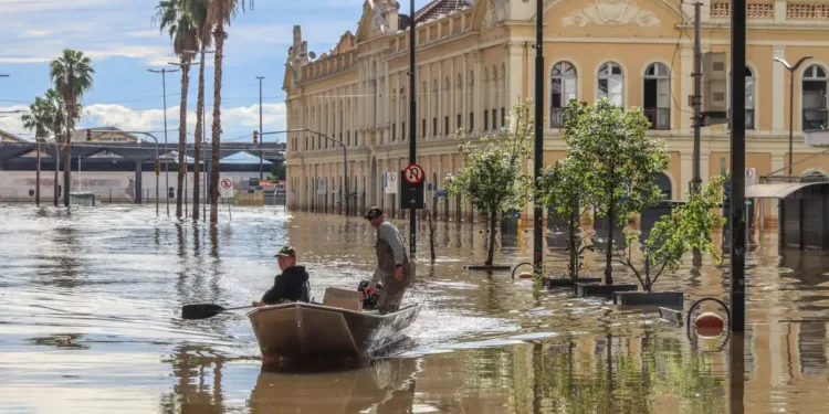 Homem e mulher em um barco enfrentando a enchente, ilustrando os impactos das chuvas e a necessidade de auxílio para reconstrução.