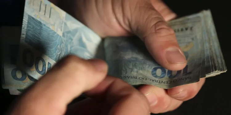 Pessoa segurando notas de 100 reais.