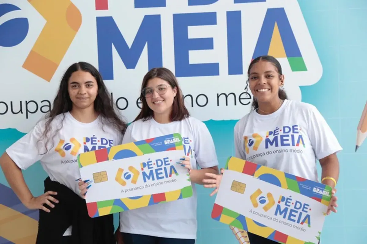 Três jovens segurando seus cartões do programa Pé-de-Meia, representando o apoio financeiro oferecido pelo programa de poupança do ensino médio