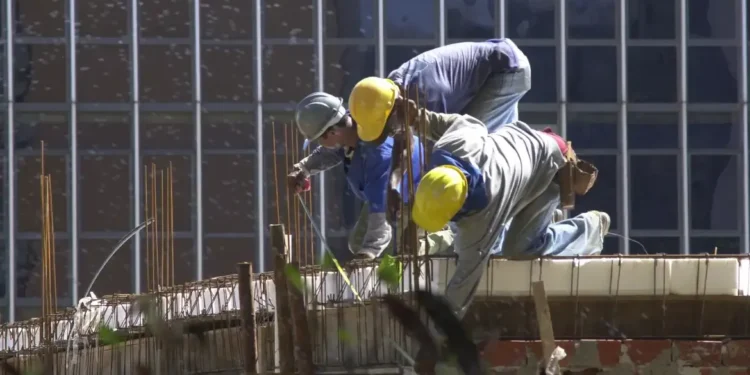 Trabalhadores da construção civil utilizando capacetes e equipamentos de segurança em uma obra.