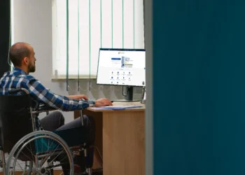 Pessoa em cadeira de rodas trabalhando em frente ao computador, acessando informações em um site.