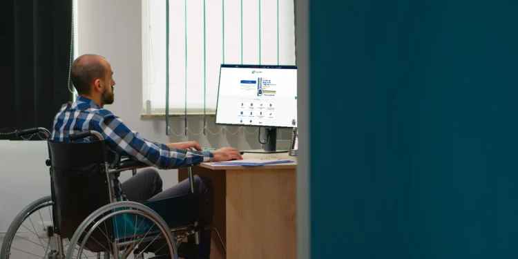 Pessoa em cadeira de rodas trabalhando em frente ao computador, acessando informações em um site.