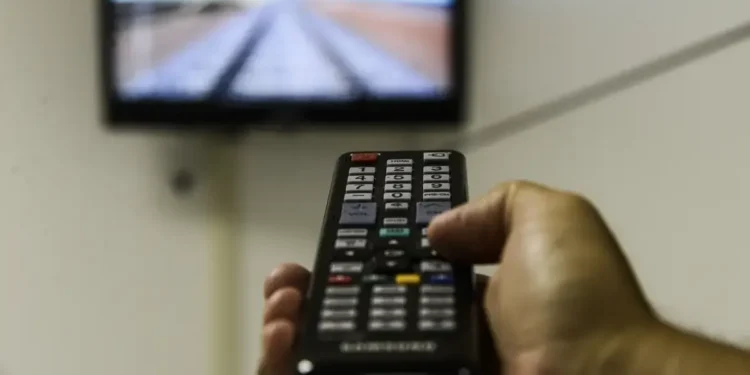 Pessoa ajustando o controle remoto para assistir à TV com sinal digital.
