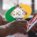 Idoso usando celular com logo de assistência social ao fundo, representando acesso a benefícios e serviços.