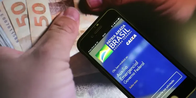 Tela do aplicativo Caixa Tem com a logo do Auxílio Emergencial, mostrando a opção de acompanhar a solicitação, com cédulas de R$ 50 ao fundo.