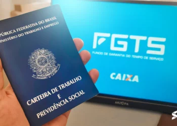 Carteira de trabalho sendo segurada à frente de uma tela com o logo do FGTS e Caixa Econômica Federal.