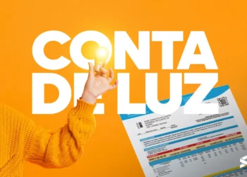 Conta de luz e economia de energia no Brasil. Mão segurando uma lâmpada acesa com uma fatura de energia ao fundo.