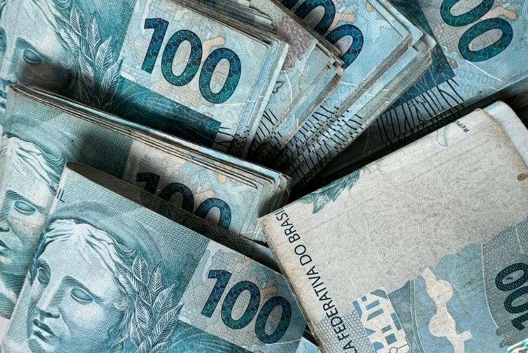 Notas de 100 reais empilhadas, representando o pagamento do 13º salário do INSS em 2025.