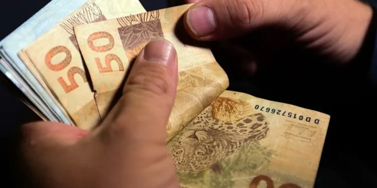 Pessoa segurando cédulas de R$ 50 e R$ 100, representando o pagamento do PIS/PASEP que será depositado na conta de milhares de brasileiros na próxima semana