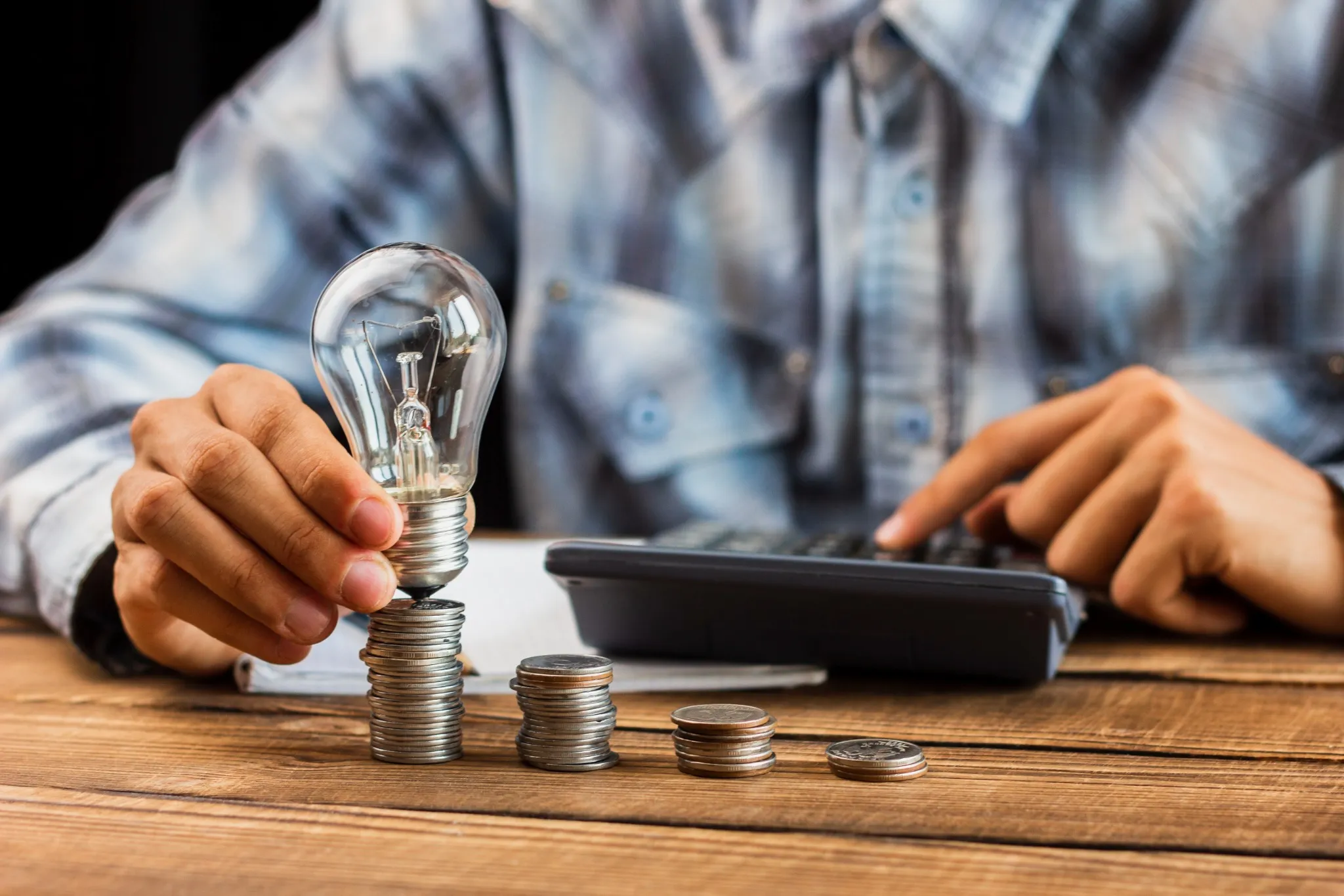 epresentação do impacto das tarifas de energia no orçamento, com um homem calculando custos e empilhando moedas.