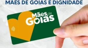 Cartão do Programa Mães de Goiás sendo segurado por uma mão, com fundo neutro e texto em destaque