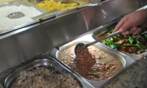 Pessoa servindo feijão em um buffet, representando o uso do Vale-Alimentação para compras em refeições.