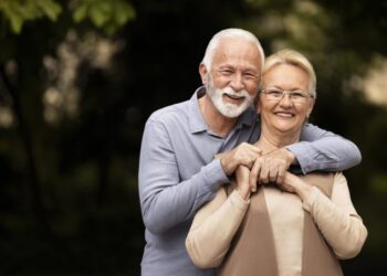 Casal de idosos sorrindo em ambiente externo representando bem-estar e qualidade de vida.