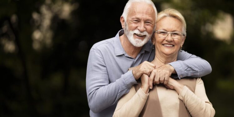 Casal de idosos sorrindo em ambiente externo representando bem-estar e qualidade de vida.