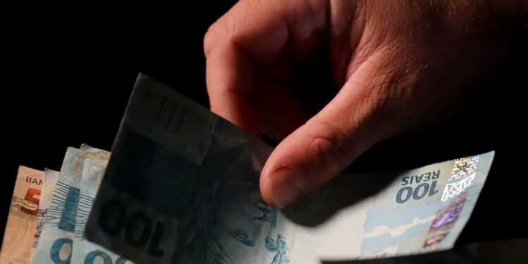 Mão segurando cédulas de dinheiro brasileiro, simbolizando crédito consignado para trabalhadores CLT.