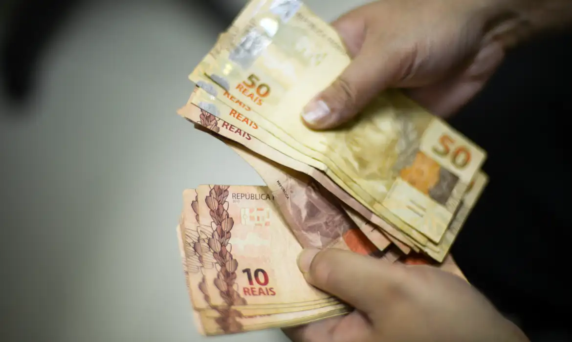 Pessoa contando notas de R$ 10 e R$ 50 representando o orçamento com salário mínimo
