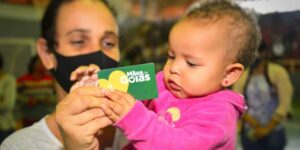 Mãe segurando o cartão do Programa Mães de Goiás junto com seu bebê no colo.