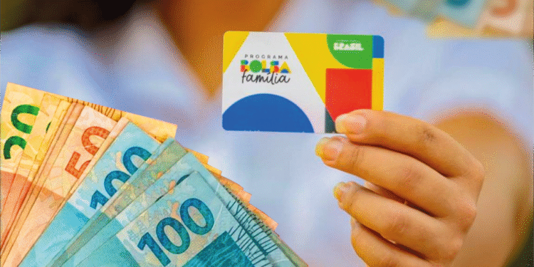 Pessoa segurando cartão do Bolsa Família com dinheiro em cédulas ao fundo