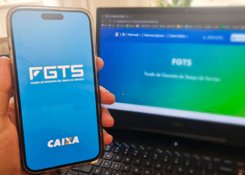 Celular mostrando o aplicativo FGTS da Caixa com notebook ao fundo
