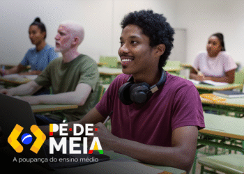 Estudante atento e feliz em sala de aula, utilizando laptop e participando das aulas com apoio do Pé-de-Meia