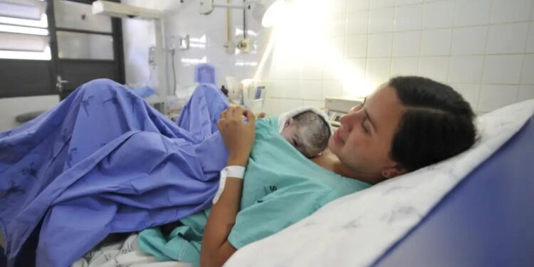 Mãe segurando seu recém-nascido na cama do hospital, simbolizando o direito à licença-maternidade.