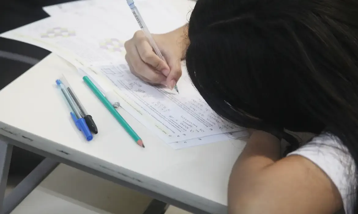 Jovem concentrada fazendo prova em cursinho popular, representando beneficiários do auxílio de R$ 200 da Rede Nacional de Cursinhos Populares.