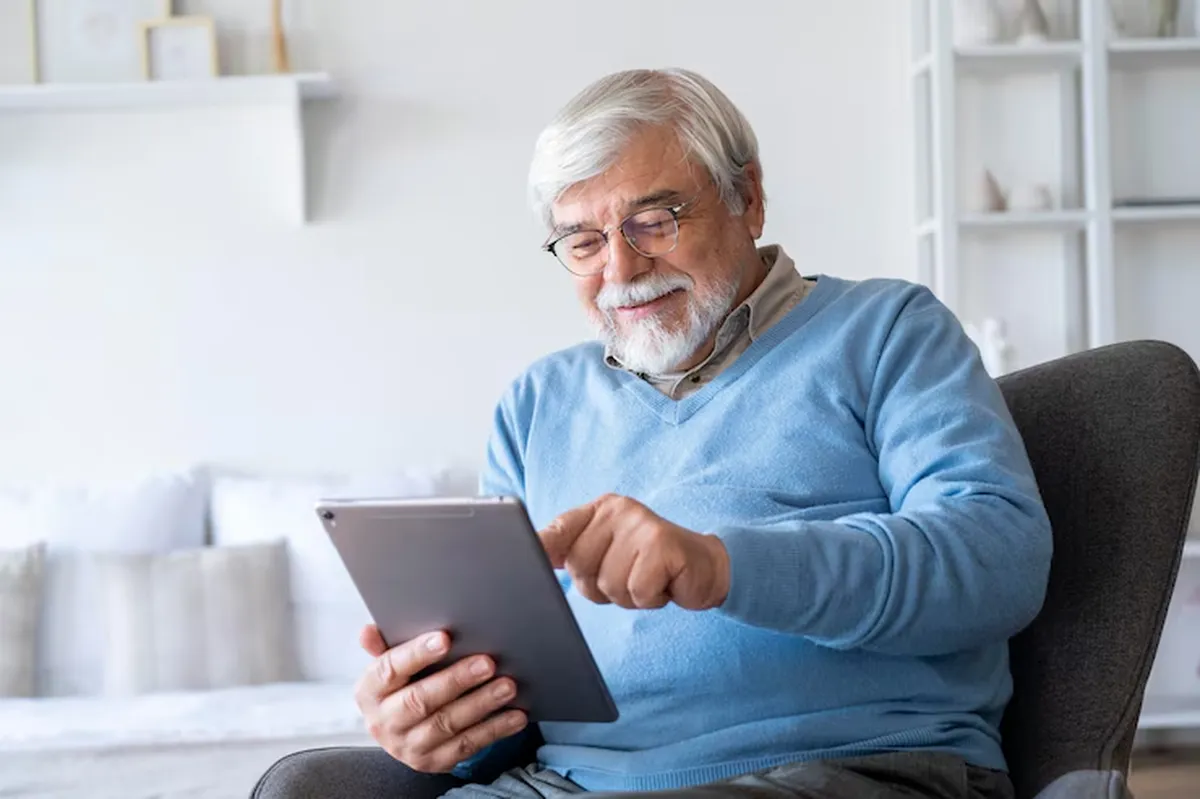 Idoso feliz usando tablet em casa para aproveitar benefícios exclusivos de 2025.