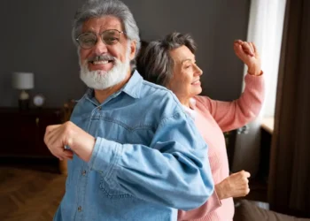 Casal de idosos felizes dançando juntos em casa, celebrando os benefícios exclusivos para idosos em 2025.