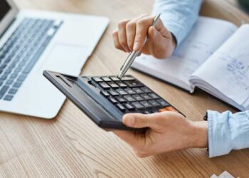 Mão feminina usando calculadora ao lado de documentos organizados, ilustrando cálculo de rescisão trabalhista.