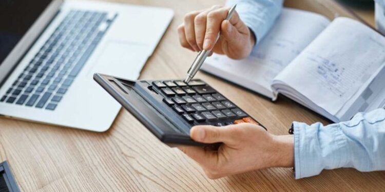 Mão feminina usando calculadora ao lado de documentos organizados, ilustrando cálculo de rescisão trabalhista.