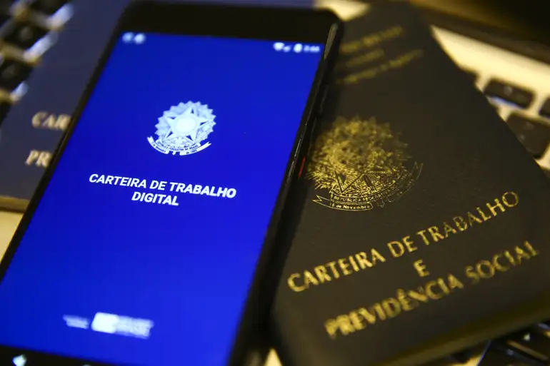Celular exibe a Carteira de Trabalho Digital ao lado da versão física do documento
