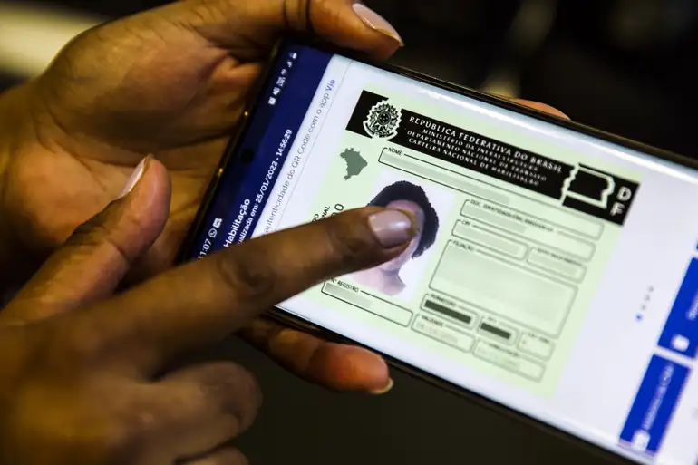 Carteira Nacional de Habilitação digital exibida em smartphone com mão tocando a tela