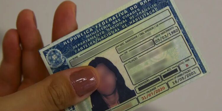 Pessoa segurando carteira nacional de habilitação (CNH) em mãos, com detalhes visíveis do documento