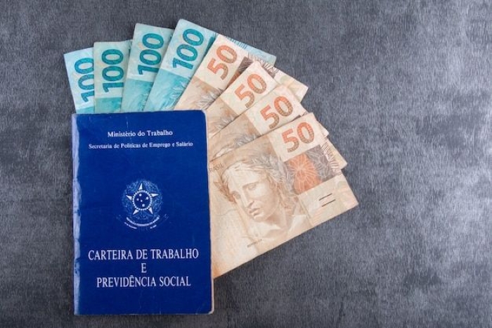 Empréstimo do Trabalhador com cédulas de 50 e 100 reais ao lado da carteira de trabalho