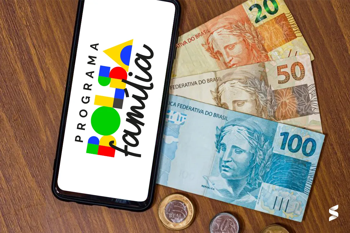 Consulta do Bolsa Família no smartphone, com cédulas e moedas de real ao fundo.