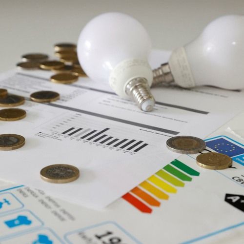 Lâmpadas e moedas sobre gráficos de consumo de energia.