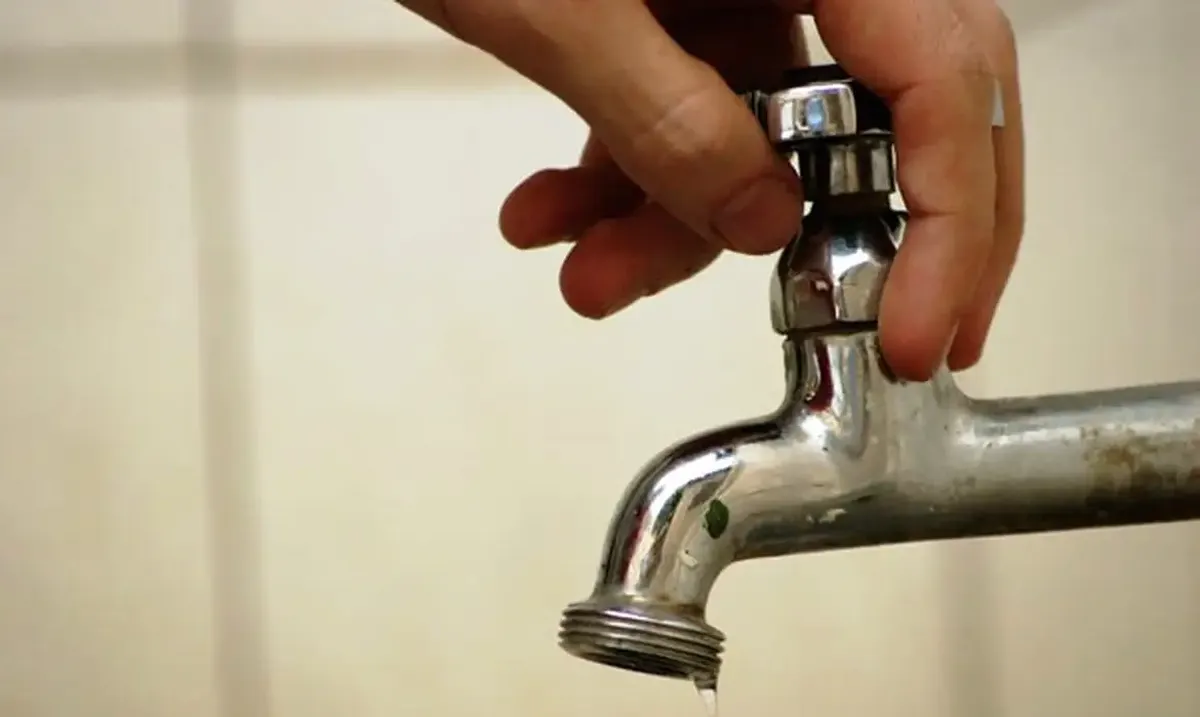 Mão fechando torneira para economizar água e evitar contas em atraso