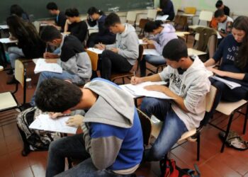 Estudantes concentrados fazendo uma prova em sala de aula.