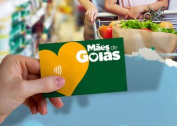 Cartão do Programa Mães de Goiás sendo segurado por uma mão, com um carrinho de supermercado ao fundo.