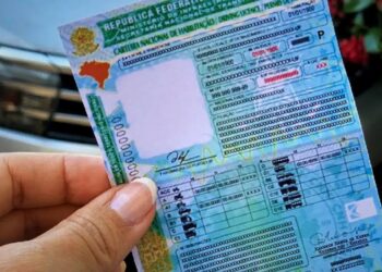 Mão segurando uma carteira nacional de habilitação brasileira com fundo desfocado.