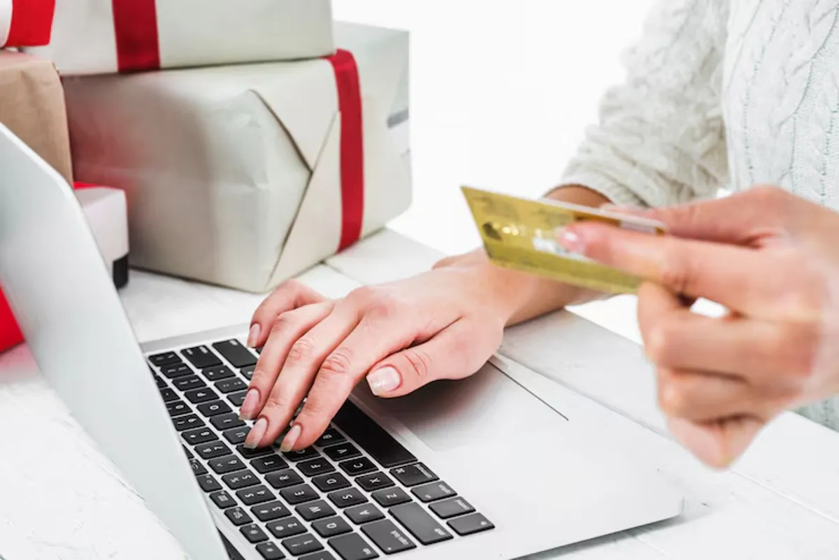 Pessoa comprando online usando cartão de crédito no computador, com presentes ao fundo