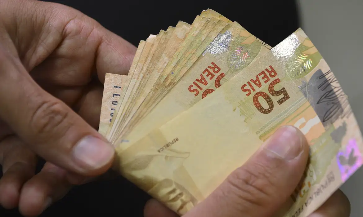 Pessoa segurando cédulas de cinquenta reais em mãos