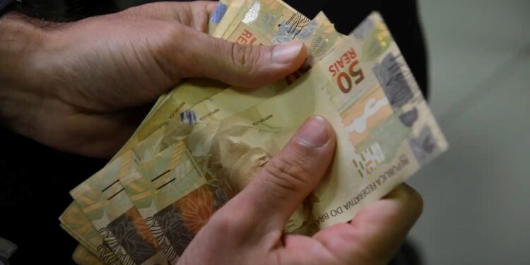 pessoa contando notas de cinquenta reais, representando o reajuste do salário mínimo no Brasil em 2025