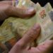 pessoa contando notas de cinquenta reais, representando o reajuste do salário mínimo no Brasil em 2025